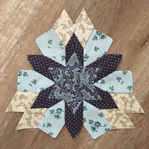 Peut inclure: Un bloc de courtepointe en forme d'&eacute;toile avec un centre violet et des pi&egrave;ces de tissu bleu, blanc et marron. Le tissu a un motif floral.