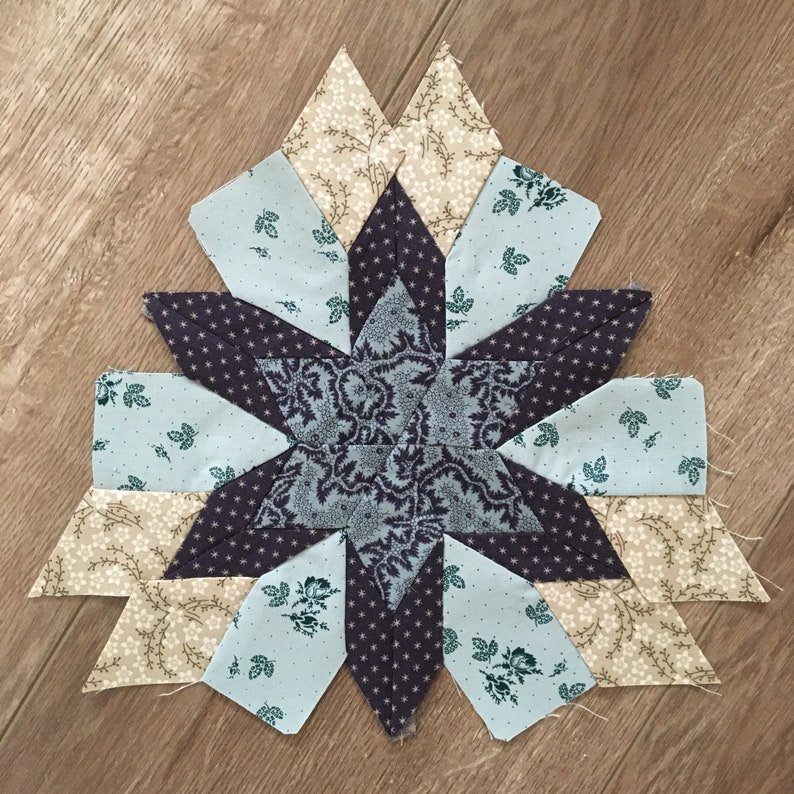 Peut inclure: Un bloc de courtepointe en forme d'&eacute;toile avec un centre violet et des pi&egrave;ces de tissu bleu, blanc et marron. Le tissu a un motif floral.