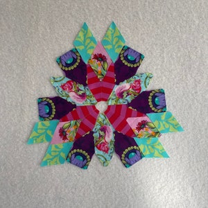Peut inclure: Un bloc de courtepointe patchwork color&eacute; avec un motif en &eacute;toile. Le bloc est compos&eacute; de diff&eacute;rents tissus dans des tons de rose, rouge, violet, vert et bleu. Le centre du bloc est une &eacute;toile blanche.