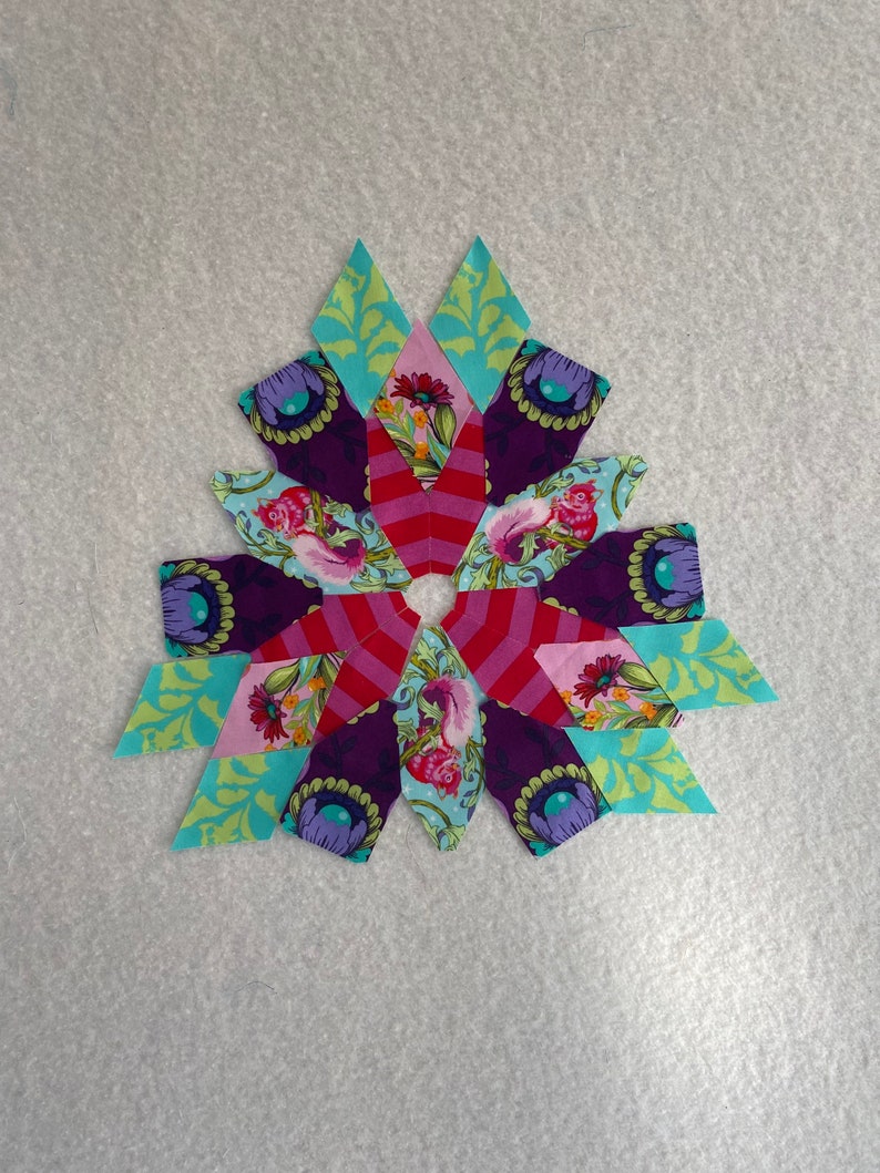 Peut inclure: Un bloc de courtepointe patchwork color&eacute; avec un motif en &eacute;toile. Le bloc est compos&eacute; de diff&eacute;rents tissus dans des tons de rose, rouge, violet, vert et bleu. Le centre du bloc est une &eacute;toile blanche.