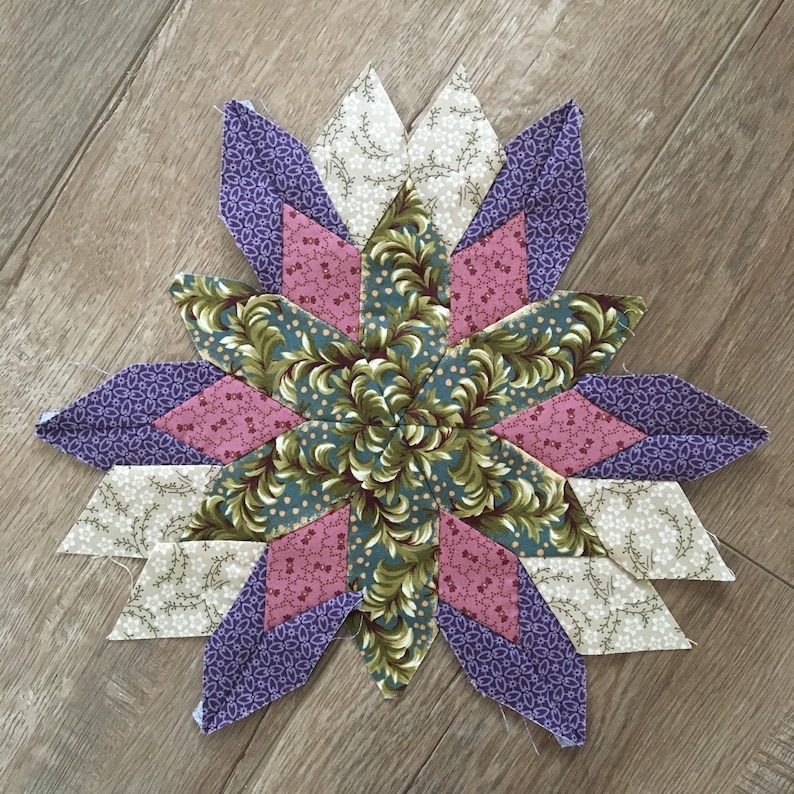 Peut inclure: Un bloc de courtepointe en patchwork en forme d'&eacute;toile, de couleur violet, rose et vert. Le bloc est compos&eacute; de diff&eacute;rents tissus &agrave; motifs floraux.