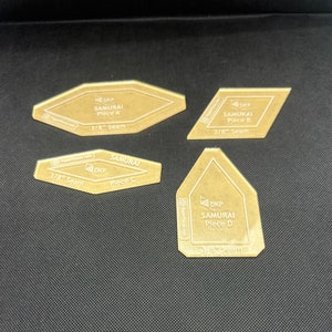 May include: Four clear plastic sewing templates for a samurai quilt pattern. The templates are labeled with the letters A, B, C, and D. Each template has a 3/8 inch seam allowance.