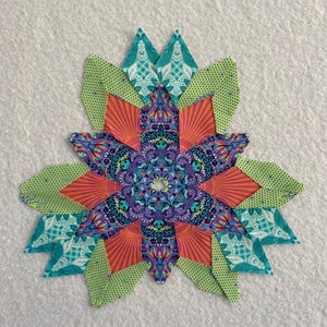Peut inclure: Un bloc de courtepointe patchwork color&eacute; avec un motif en &eacute;toile. Le bloc est compos&eacute; de diff&eacute;rents tissus dans des tons de vert, orange, violet et bleu. Le centre du bloc pr&eacute;sente un motif de mandala d&eacute;taill&eacute;.