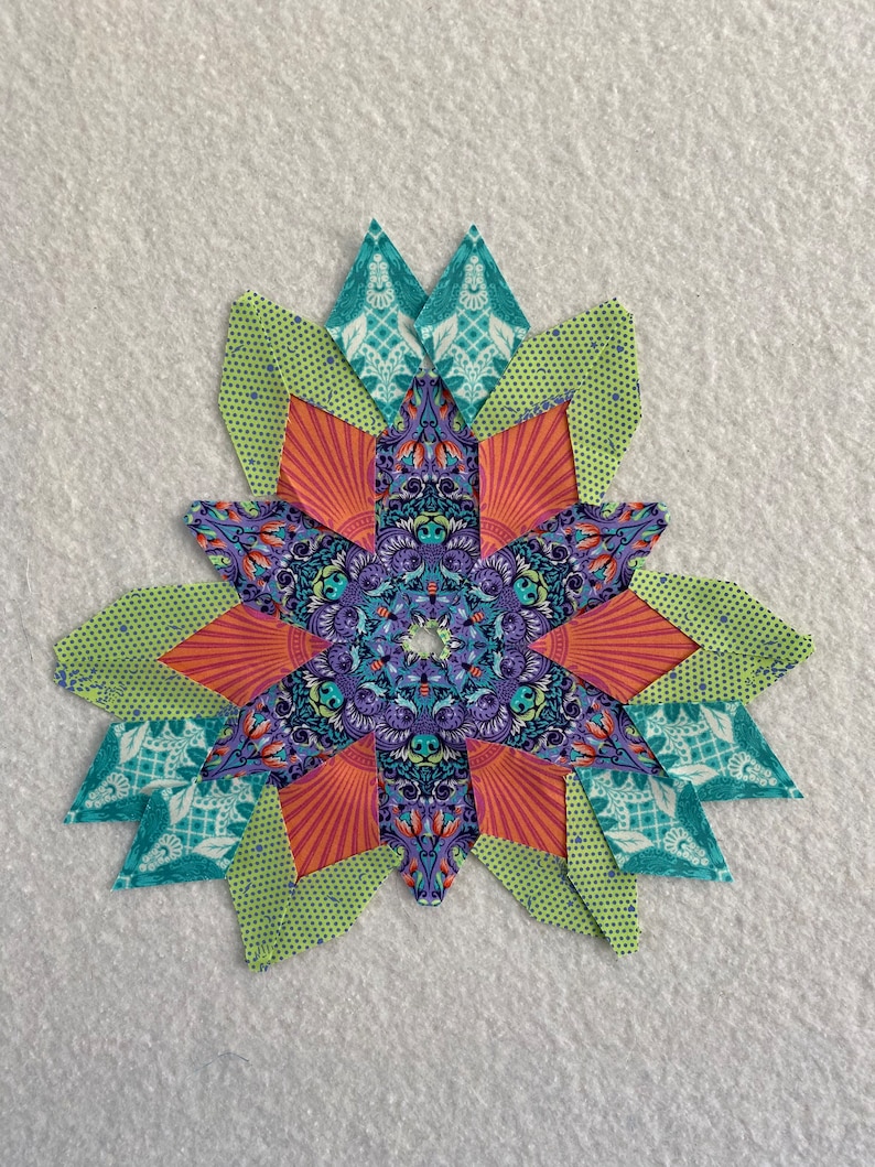 Peut inclure: Un bloc de courtepointe patchwork color&eacute; avec un motif en &eacute;toile. Le bloc est compos&eacute; de diff&eacute;rents tissus dans des tons de vert, orange, violet et bleu. Le centre du bloc pr&eacute;sente un motif de mandala d&eacute;taill&eacute;.