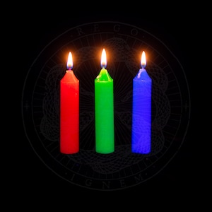Puede incluir: Tres velas, una roja, una verde y una azul, están encendidas y ardiendo frente a un círculo blanco y negro con las palabras "REGO. IGNEM." alrededor del borde.