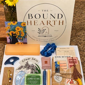 Puede incluir: Un set de regalo de The Bound Hearth que incluye una tarjeta de girasoles y gato negro, un coletero azul, un registro de lectura, tarjetas de reseñas de libros, un marcapáginas de metal con cuentas, toallitas faciales y un bolígrafo azul.