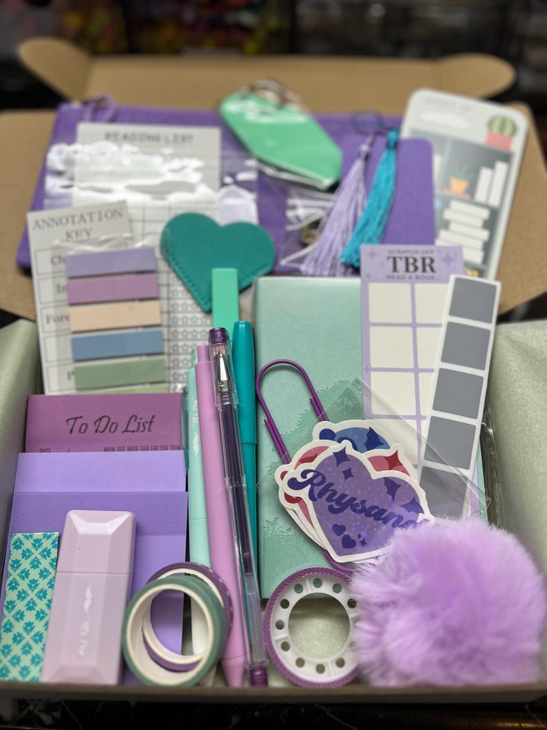 May include: A stationery gift box containing a purple To Do List pad, an annotation key card, a scratch-off TBR card, a green notebook, pens, washi tape rolls, a heart-shaped tag, a large purple paperclip, a fuzzy pom-pom, and a Rhysand sticker.