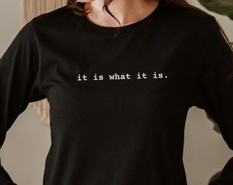 May include: A black long-sleeved shirt with the text "it is what it is." printed in white on the front.