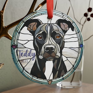 May include: A round glass ornament with a stained glass design of a black and white dog. The dog's name, "Teddy", and the year "2023" are written in purple text on the ornament.