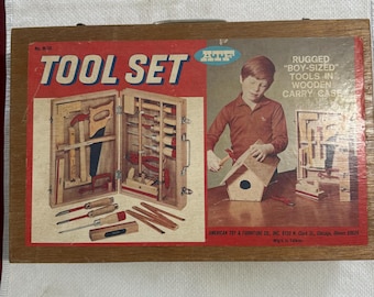 May include: Vintage wooden tool set with a red and white graphic. The tool set includes a variety of small tools and is labeled "RUGGED 'BOY-SIZED' TOOLS IN WOODEN CARRY CASE". The box features an illustration of a boy using the tools.