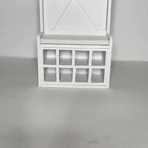 May include: White wooden storage bench with a shelf and a decorative X-shaped back. The bench has a cushion and a row of knobs along the top.