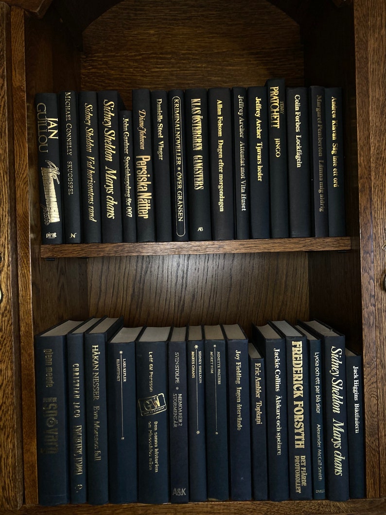 K&ouml;nnte beinhalten: Ein B&uuml;cherregal gef&uuml;llt mit schwarzen B&uuml;chern mit goldenen Lettern. Die B&uuml;cher sind nach Autor und Titel geordnet. Die B&uuml;cher sind alle in verschiedenen Gr&ouml;&szlig;en und Formen. Das B&uuml;cherregal ist aus Holz und hat eine dunkelbraune Oberfl&auml;che.
