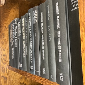 K&ouml;nnte beinhalten: Ein B&uuml;cherregal gef&uuml;llt mit schwarzen Hardcover-B&uuml;chern. Die Titel der B&uuml;cher sind sichtbar, darunter "Manga Liv", "Stephen King Mardrommar", "Bjorn Hellberg Paria", "Henning Mankell Den Orolige Mannen", "Denise Mina Blodsarv" und "Carste Jense Vi, de drunkna".