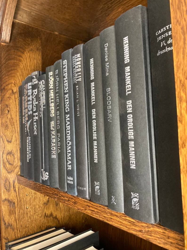K&ouml;nnte beinhalten: Ein B&uuml;cherregal gef&uuml;llt mit schwarzen Hardcover-B&uuml;chern. Die Titel der B&uuml;cher sind sichtbar, darunter "Manga Liv", "Stephen King Mardrommar", "Bjorn Hellberg Paria", "Henning Mankell Den Orolige Mannen", "Denise Mina Blodsarv" und "Carste Jense Vi, de drunkna".