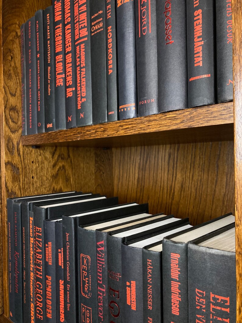 K&ouml;nnte beinhalten: Ein B&uuml;cherregal gef&uuml;llt mit schwarzen B&uuml;chern mit roten Titeln. Die B&uuml;cher sind in Reihen angeordnet und alle gleich gro&szlig;. Das B&uuml;cherregal ist aus Holz und hat eine dunkelbraune Oberfl&auml;che.