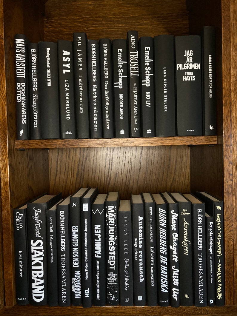 K&ouml;nnte beinhalten: Ein B&uuml;cherregal mit schwarzen B&uuml;chern mit wei&szlig;en Texttiteln. Die B&uuml;cher sind in zwei Reihen angeordnet. Die obere Reihe enth&auml;lt Titel wie "Asyl", "The Step After", "The Sharpener", "The Night Wanderer", "The Multiple Murderer", "Brother Jacob", "On the Heart Still", "Nine Lives", "The Stalker", "The Pilgrim", "Gone Forever". Die untere Reihe enth&auml;lt Titel wie "Eleven Minutes", "Family", "The Son of Glomer", "Trophy Collector", "De Hatsika", "The Doctor as Patient", "Antonia's Revenge", "Stella & Sebastian", "Marijungstedet", "Trophy Collector", "The Good Host", "The World of Melis".