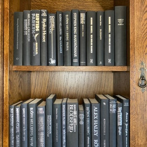 K&ouml;nnte beinhalten: Ein B&uuml;cherregal gef&uuml;llt mit schwarzen B&uuml;chern mit wei&szlig;en Texttiteln. Die B&uuml;cher sind in zwei Reihen angeordnet. Die obere Reihe hat 15 B&uuml;cher und die untere Reihe 13 B&uuml;cher. Die B&uuml;cher sind alle unterschiedlich gro&szlig; und haben unterschiedliche Titel.