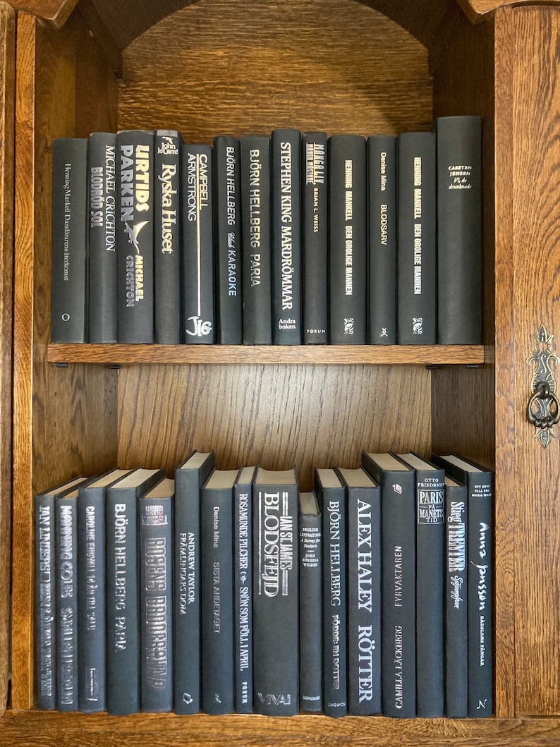 K&ouml;nnte beinhalten: Ein B&uuml;cherregal gef&uuml;llt mit schwarzen B&uuml;chern mit wei&szlig;en Texttiteln. Die B&uuml;cher sind in zwei Reihen angeordnet. Die obere Reihe hat 15 B&uuml;cher und die untere Reihe 13 B&uuml;cher. Die B&uuml;cher sind alle unterschiedlich gro&szlig; und haben unterschiedliche Titel.