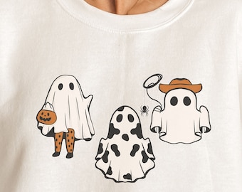 May include: White sweatshirt with a graphic of three ghosts wearing different costumes. The ghosts are wearing a cowboy hat, a pumpkin, and a cow print.