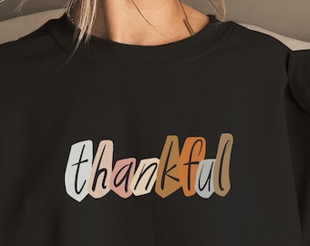 Puede incluir: Sudadera negra con la palabra "agradecido" escrita en letras de colores.