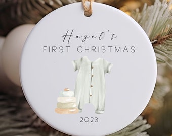 Puede incluir: Adorno navideño de cerámica blanca con un mono verde, una pila de anillos de madera y el texto "Hazel's First Christmas 2023".