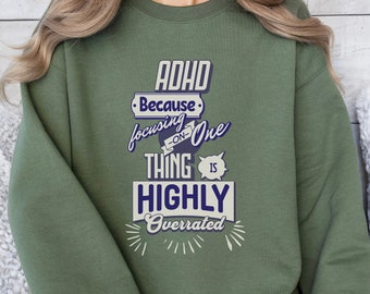 May include: Green sweatshirt with a white and blue graphic that says "ADHD Because focusing on one thing is highly overrated".