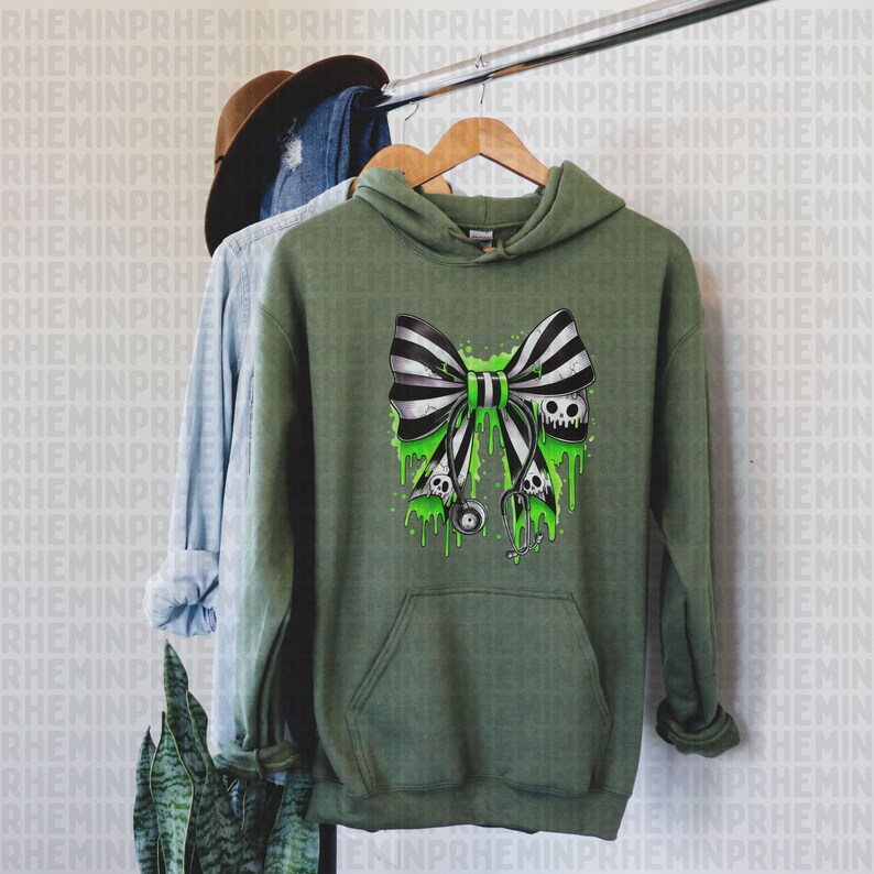Op de afbeelding: Olijfgroene hoodie met een zwart-wit gestreept strikdesign, met schedels en groene druipaccenten. De hoodie heeft een voorzak en een capuchon met trekkoord. Het ontwerp bevat een stethoscoop.