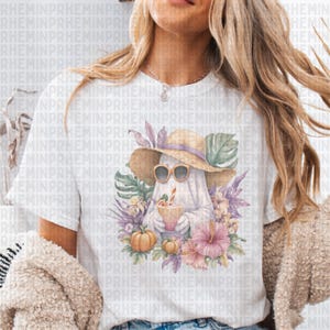 May include: White t-shirt featuring a whimsical ghost design. The ghost wears sunglasses and a straw hat, holding a tropical drink. Surrounded by pumpkins, flowers, and foliage, the design has a fall and tropical theme.