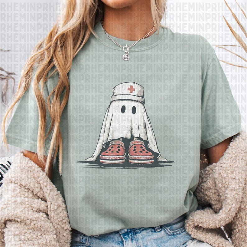 Pode incluir: Camiseta verde s&aacute;lvia com um fantasma de desenho animado usando um gorro de enfermeira com uma cruz vermelha e tamancos vermelhos. O fantasma est&aacute; envolto em um len&ccedil;ol branco com dois olhos pretos.