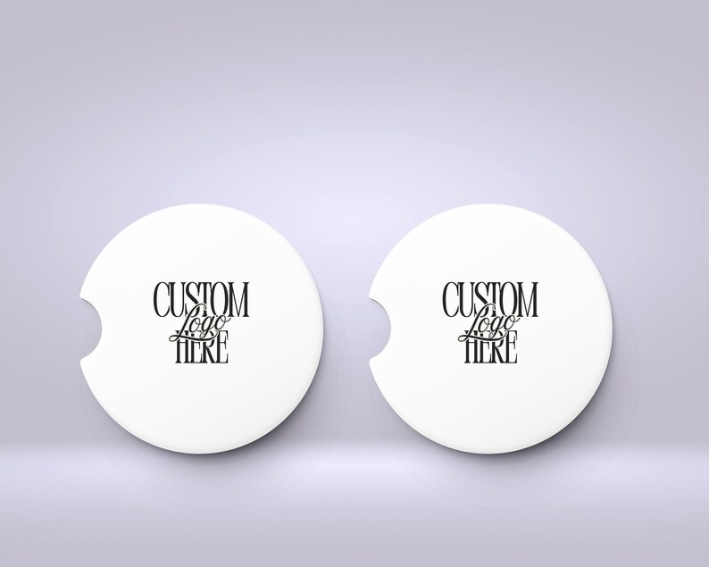 May include: Two white car coasters with a curved notch and the text "CUSTOM Logo HERE" in black script. The coasters are round and sit on a light purple background.