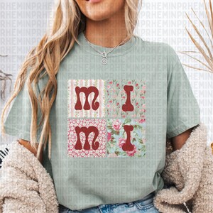 May include: A light green t-shirt with a patchwork design featuring the word "Mimi" in red letters. Each letter is surrounded by a different floral pattern.