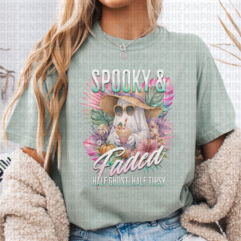 May include: A light green t-shirt with a graphic featuring a ghost wearing sunglasses and a straw hat, holding a drink. The text reads "Spooky & Faded, Half Ghost, Half Tipsy". The design includes tropical flowers and pumpkins.