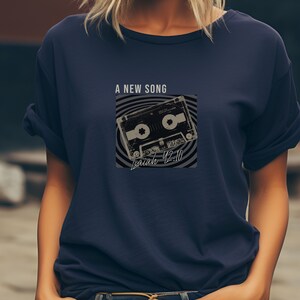 May include: A navy blue t-shirt with a vintage cassette tape graphic and the text "A New Song" and "Isaiah 42:10".