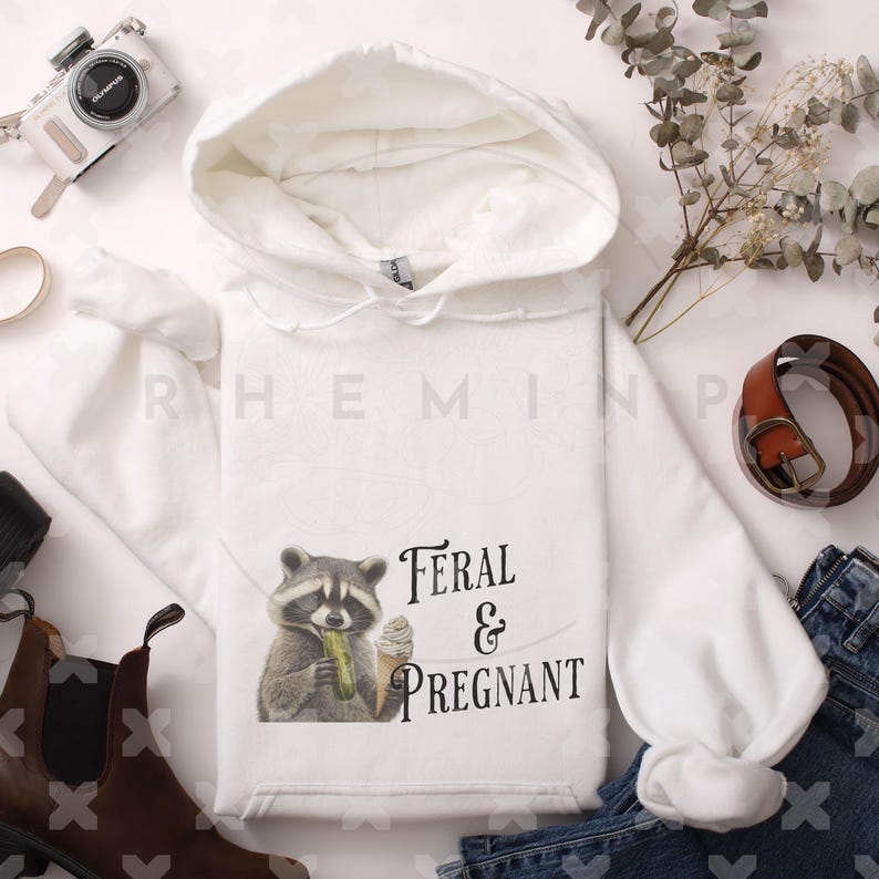 Op de afbeelding: Witte hoodie met een wasbeer die een augurk en ijs eet. De tekst "Feral & Pregnant" staat op de hoodie gedrukt.