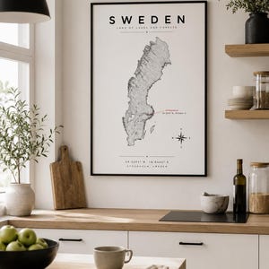 Könnte beinhalten: Ein gerahmtes Wandposter mit einer schwarz-weißen Landkarte von Schweden und dem Text SWEDEN LAND OF LAKES AND FORESTS. Die Karte enthält eine Windrose, den rot markierten Standort Stockholm sowie Koordinaten am unteren Rand des Drucks.