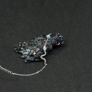 May include: A silver snake pendant necklace with a delicate chain. The snake design features a light blue gemstone at the head and is adorned with small, sparkling crystals. The necklace is displayed on a dark, textured surface.