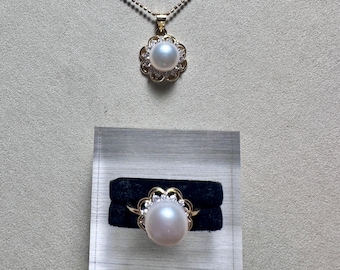 May include: A gold-toned necklace and ring set. The necklace features a pendant with a white pearl surrounded by a floral design with small clear stones. The ring has a similar design with a large pearl and gold band.