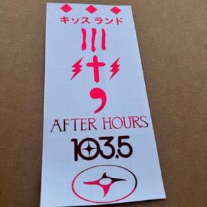 May include: A rectangular sticker with a white background and red text. The sticker features Japanese characters, the words "AFTER HOURS" and "103.5", and a stylized design. The sticker is on a brown surface.