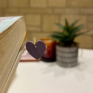 May include: A purple heart-shaped bookmark attached to a gold wire bookmark holder.