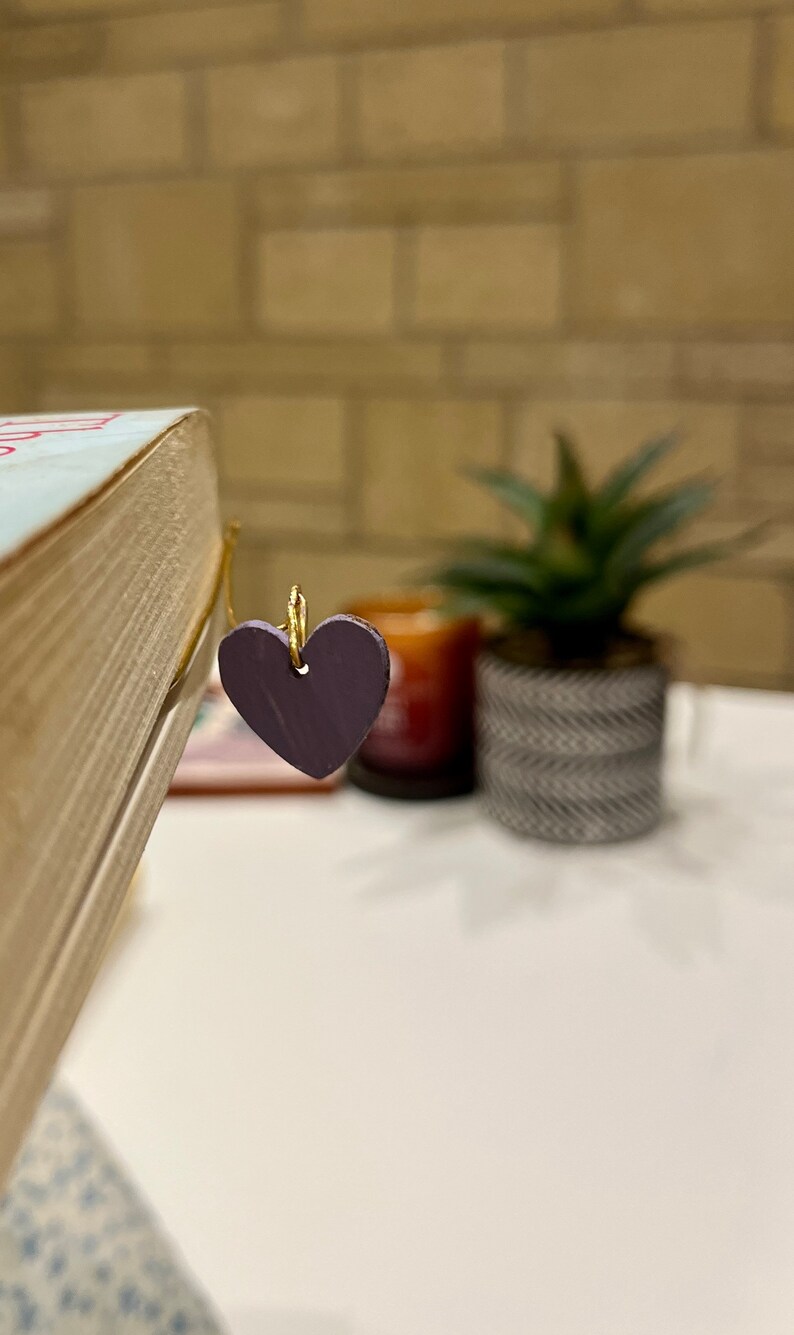 May include: A purple heart-shaped bookmark attached to a gold wire bookmark holder.