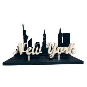 May include: A black and white 3D printed model of the New York City skyline with the word "New York" in white lettering.