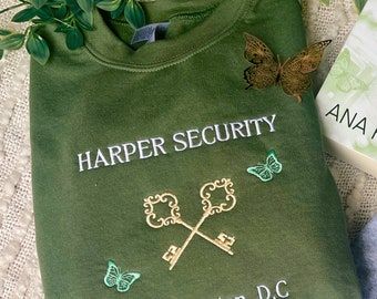 Puede incluir: Una sudadera verde con el texto "HARPER SECURITY" y "Washington, D.C." bordado en blanco. La sudadera presenta un diseño bordado en oro de dos llaves cruzadas y varias mariposas bordadas.