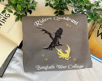 May include: Gray sweatshirt with embroidered text "Riders Quadrant" and "Basgiath War College". The design features a black dragon and a yellow dragon with stars.