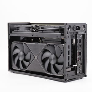 May include: Black computer case with two large fans and a series of ports. The case has a rectangular shape with a mesh side panel. The fans are circular with multiple blades. The case is designed for computer components.