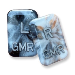 May include: Two rectangular resin pieces with marbled black, white, and silver designs. One piece has the letter "L" and the letters "GMR" in silver. The other has the letter "R" and the letters "GMR".