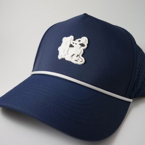 May include: A navy blue baseball cap with a white rope trim and a white embroidered cartoon dog on the front.