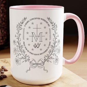 May include: White ceramic mug with a pink rim and handle. The mug features a black and white illustration of a religious icon with the text "O Mary, Conceived Without Sin Pray for Us Who Have Recourse to Thee".