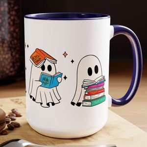 Op de afbeelding: Een witte keramische koffiemok met een blauwe rand en handvat. De mok heeft een ontwerp met drie geesten die boeken lezen. Eén geest draagt een boek op zijn hoofd, een ander houdt een boek vast met de titel "A Court of Thorns and Roses", en de derde geest houdt een stapel boeken vast.