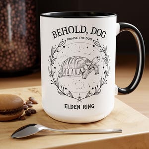 May include: A white ceramic mug with a black handle and the text "But First, Coffee" in a black, bold font. The mug is on a white surface.