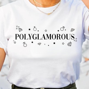 Op de afbeelding: Wit T-shirt met de tekst "Polyglamorous" in zwart gedrukt. De tekst wordt omringd door kleine zwarte sterren en diamant- en ringsymbolen.